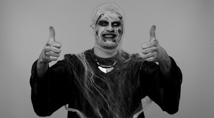 Sinister man with scary Halloween zombie makeup raises thumbs up agrees with something or gives...