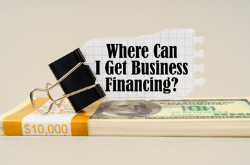 On the table are dollars, a paper clip and torn paper with the inscription - Where Can I Get Business Financing