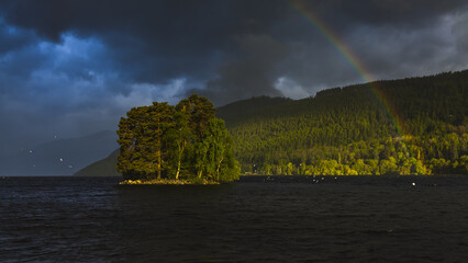 A sunrise rainbow over a lonely islet in a lake in Scotland.j