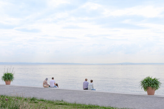 Two seated tourist couples look out onto the bright lake, copyspace