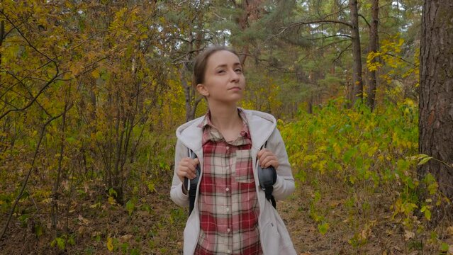 Front view of young woman with backpack walking in autumn park, forest - wide angle steadicam shot. Active outdoor lifestyle, leisure time, freedom and adventure concept