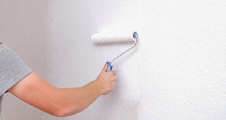 A man is painting vinyl wallpaper with a velour roller for painting with white paint. Renovation of the room.