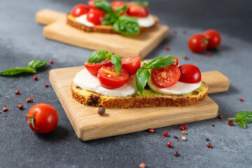 Juicy aromatic caprese sandwich with basil leaves, cherry tomatoes and mozzarella cheese on dark rustic background close up. Healthy tasty food concept.