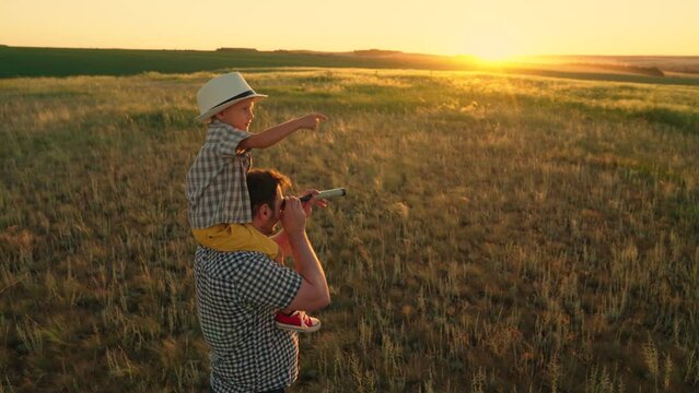 Travelers, son, dad play together at sunset. Son, boy, sits on his fathers shoulders, playing travelers, looking through spyglass. Happy family is resting in park, Child dream of discovery, adventure