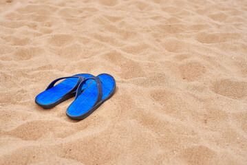 Bright blue men's rubber slates stand on the beautiful yellow sea sand. The concept of recreation in hot countries. Beach holidays. Clean sand.