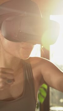 CLOSE UP: Sporty Asian woman having fun boxing at home using modern VR goggles. Sports and virtual reality concept. Asian lady doing boxing exercises at home with futuristic technology virtual device.