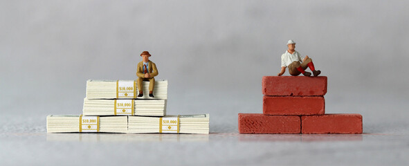 A miniature man sitting on a $100 bill and a miniature man sitting on a red brick. The concept of...