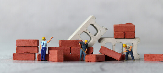 Miniature people and a pile of red bricks. The concept of the gap between rich and poor.
