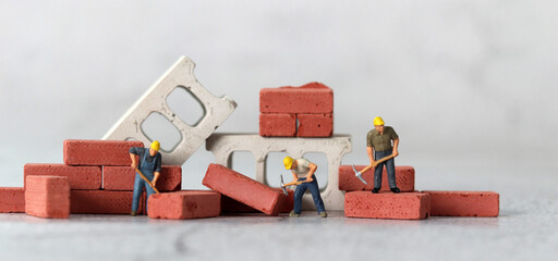 Miniature people and a pile of red bricks. The concept of the gap between rich and poor.
