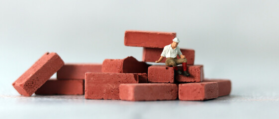 A miniature man sitting on a pile of red bricks. The concept of the gap between rich and poor.
