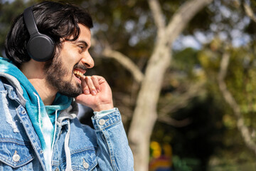 Young latin man listening to music outdoors with headphones. Expression of happiness, winning attitude.