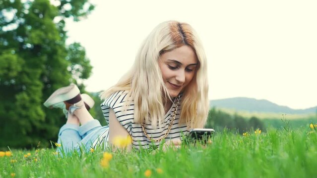 young European girl lying on the grass and typing in her phone. full shot outdoor. High quality 4k footage
