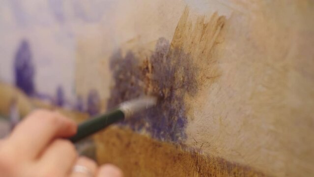 Close-up of artist hand holding the paint brush and drawing the rural landscape. female hand is rubbing the paints on the canvas. impressionism art.