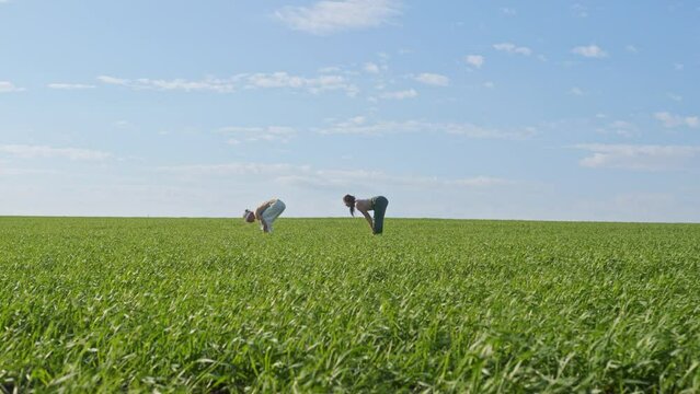 Young people practice yoga on green field against blue sky. Young people practice yoga on green field. Man and woman concentrate on asana and unite with nature on windy day against blue sky from
