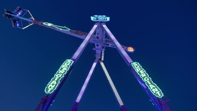 Outdoor sunny low angle view of  pendulum amusement ride, rotate and swing down and up against night sky. 