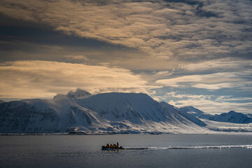 2022-07-16 A SMALL ZODIAC MOTORING IN FRONT OF A SNOW COVERED MOUNTAIN RANGE NEAR SVALBARD NORAY IN THE ARCTIC © Michael J Magee