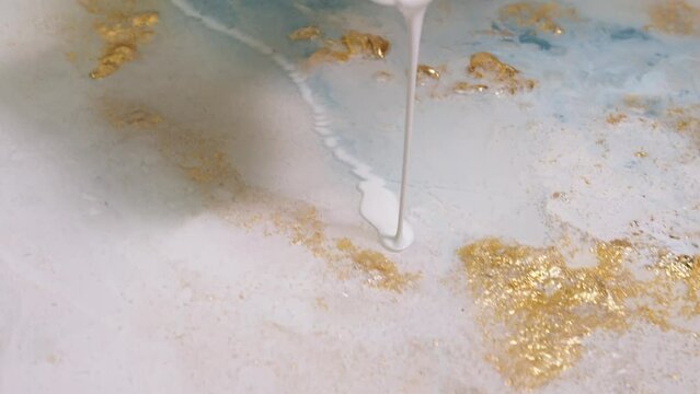 Close-up of pouring white-colored paint on the canvas. mixing acrylic paints with epoxide resin in fluid art technique.