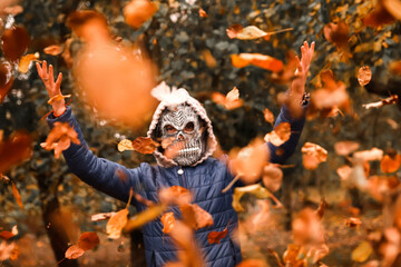 Defocus Halloween people. Person in grim reaper mask raising hand and throwing leaves. Many flying...