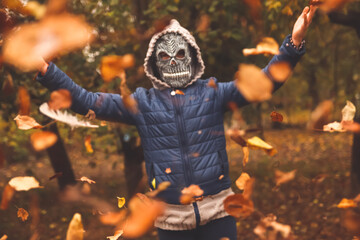 Defocus Halloween people. Person in grim reaper mask raising hand and throwing leaves. Many flying orange, yellow, green dry leaves. Copy space. Fall park. Demon costume. Vintage tone. Out of focus