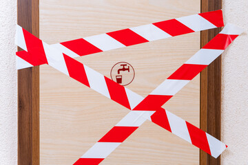 Wooden door with a tap and glass pattern, which is blocked by signal tape. Entrance to the room is prohibited due to an accident or due to some kind of technical malfunction
