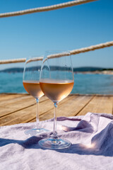 Glasses of cold rose wine from Provence served outdoor on wooden yacht pier with view on blue water and white sandy beach Plage de Pampelonne near Saint-Tropez, France