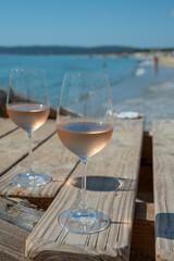 Glasses of cold rose wine from Provence served outdoor on wooden yacht pier with view on blue water and white sandy beach Plage de Pampelonne near Saint-Tropez, France