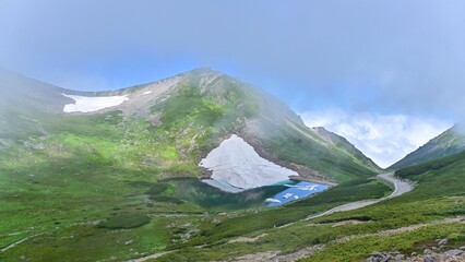 Fototapeta premium 富士見岳から見おろす霧に包まれた雪渓と不消ヶ池のコラボ情景＠長野