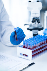 Doctor hand taking a blood sample tube from a rack with machines of analysis in the lab background,...