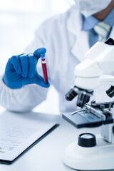 Doctor hand taking a blood sample tube from a rack with machines of analysis in the lab background,...