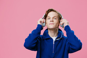 a handsome, cute guy in a blue sweater puts headphones on his head to listen to music. Judge photo against a plain background with space for an advertising layout