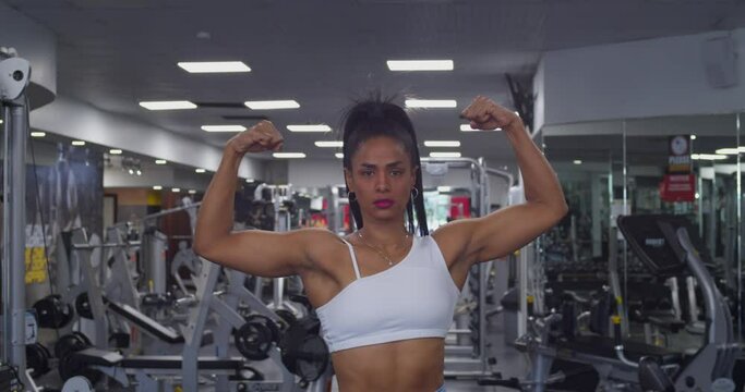 Strong female bodybuilder in sports wear flexing her biceps at the gym