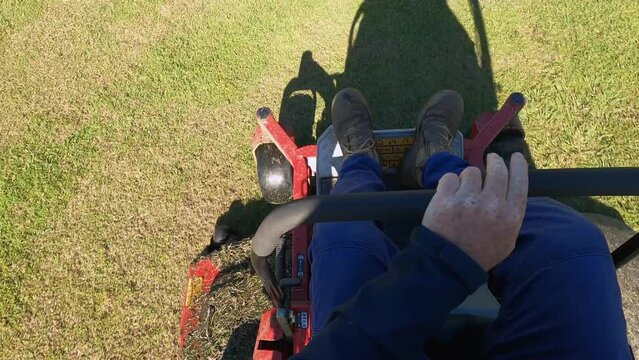A blue-collar worker finishes mowing a sports oval and turns off his ride on lawn mower.