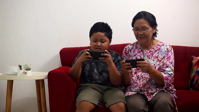 Asian grandmother playing games on smartphone with her grandson at home
