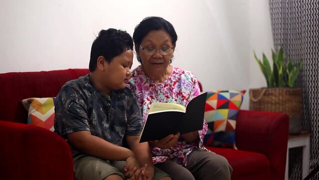 Young asian boy and asian grandmother reading book at home. Side view with copyspace