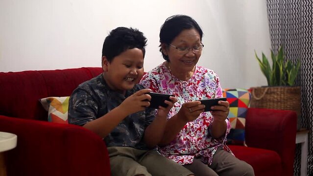 Asian grandmother playing games on smartphone with her grandson and granddaughter in living room at home