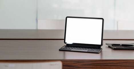 Fototapeta premium Blank white screen digital tablet with magic keyboard on wooden table in meeting room.