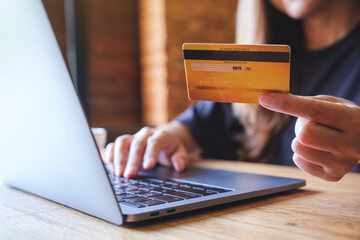 Closeup image of a woman holding credit cards while using laptop computer for online payment