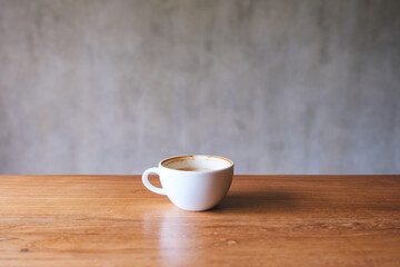 A white cup of hot coffee on wooden table with concrete wall background