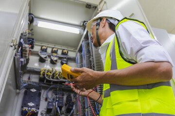 Electrician installing electric cable wires and fuse switch box. Multimeter in hands of electricians detail.Electrician repairing electrical control cabinets.
