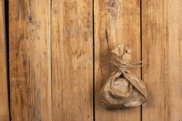 Tied paper bag against a wooden background. Brown paper bag tied with string. Rough cracked boards. Copy space for text and design elements. Top view. Selective focus.