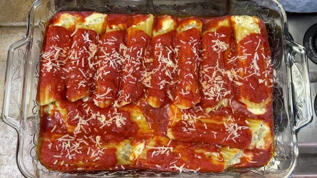 4K HD video zooming in on on freshly baked stuffed manicotti covered in marinara sauce and sprinkled with parmesan cheese. Above view.
