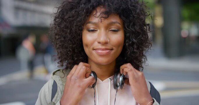 Portrait of a trendy young black woman with a carefree and cool attitude standing in the city outdoors. Beautiful, confident and cheerful african student smiling with curly afro hair and headphones