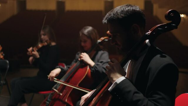 rehearsal of symphonic orchestra in opera house, cellists are playing on scene of philharmonic hall