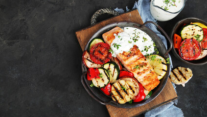 Salmon steak with vegetables and white sauce on dark background.