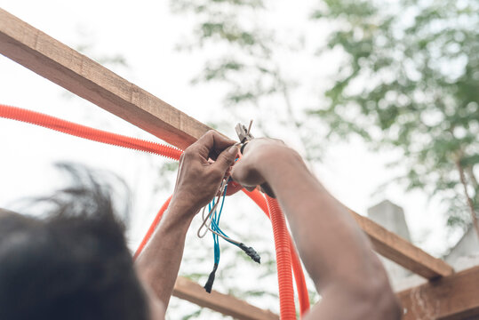 A Man Cutting Excess Wiring With A Pair Of Combination Pliers. Wires Jutting Out From A Plastic Junction Box Installed On Rafters.