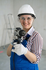 Portrait of Smiling Female Builder with Puncher in Hands Posing by the Ladder and Concrete Wall. Vertical View