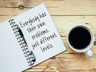 Open notebook with text "Everybody has their own problems, just different levels" and a cup  of coffee on wooden background.
