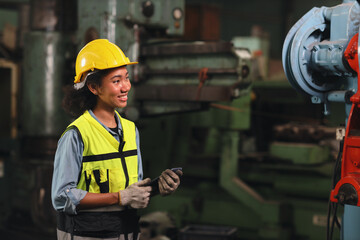 Technician engineer or worker in protective uniform standing and holding tablet while controlling operation or checking industry machine process with hardhat  at heavy industry manufacturing factory