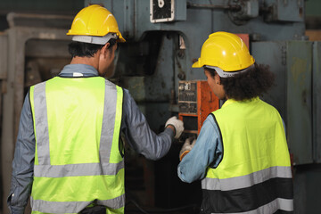 Rear view technician engineer or worker man and woman in protective suit standing and repairing operation or check industry machine process with safety hardhat at heavy industry manufacturing factory
