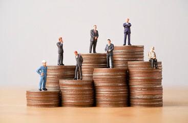 Many Business miniature figure standing on coins stacking for different income and salary in each...